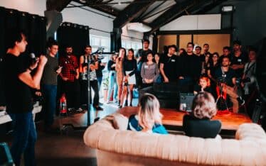 A dynamic group of people gathered in an indoor event space, attentively listening to a speaker at the front, illustrating the concept of 'building your tribe' in a community or business setting