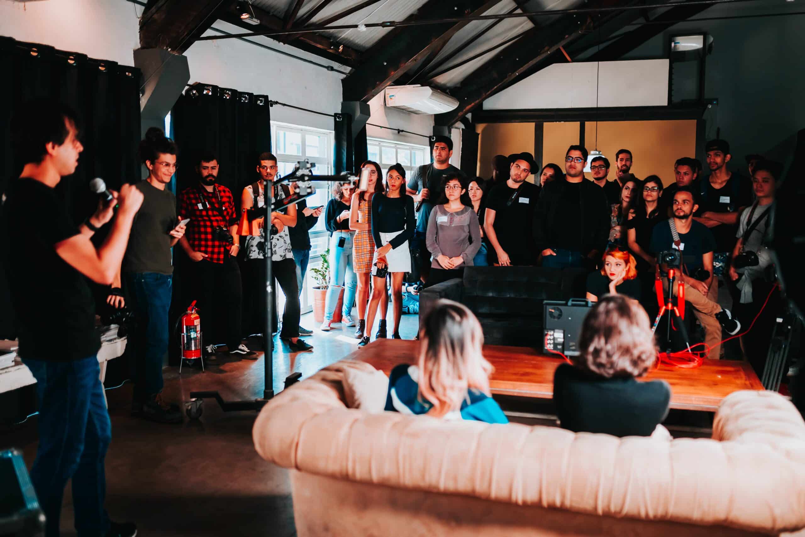 A dynamic group of people gathered in an indoor event space, attentively listening to a speaker at the front, illustrating the concept of 'building your tribe' in a community or business setting