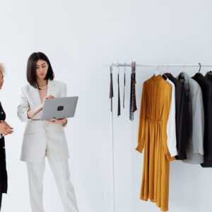 Two entrepreneurs in a modern fashion studio, one holding a laptop, discussing strategies for Brand Desire Mastery in Social Media, beside a rack of stylish clothing.