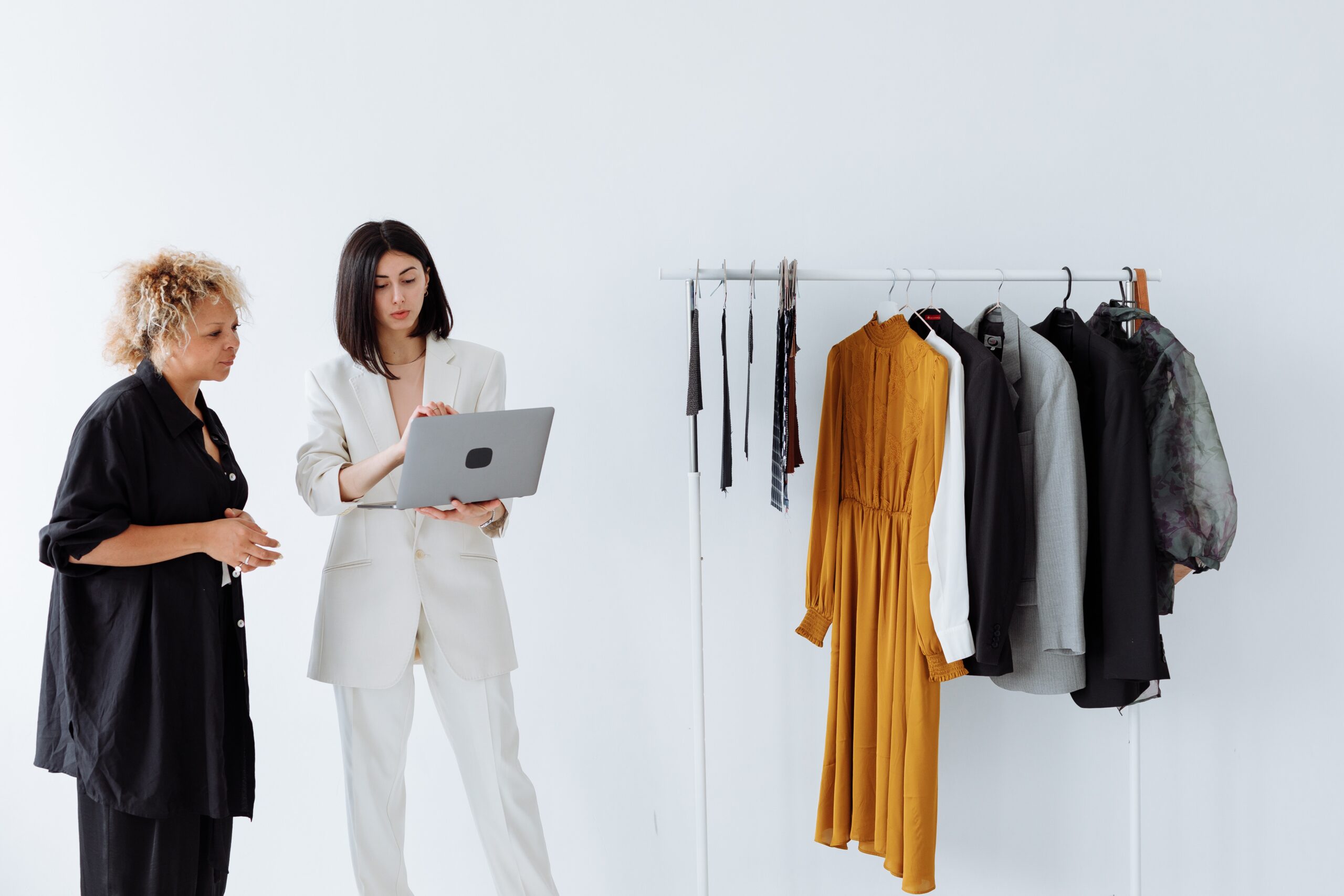 Two entrepreneurs in a modern fashion studio, one holding a laptop, discussing strategies for Brand Desire Mastery in Social Media, beside a rack of stylish clothing.