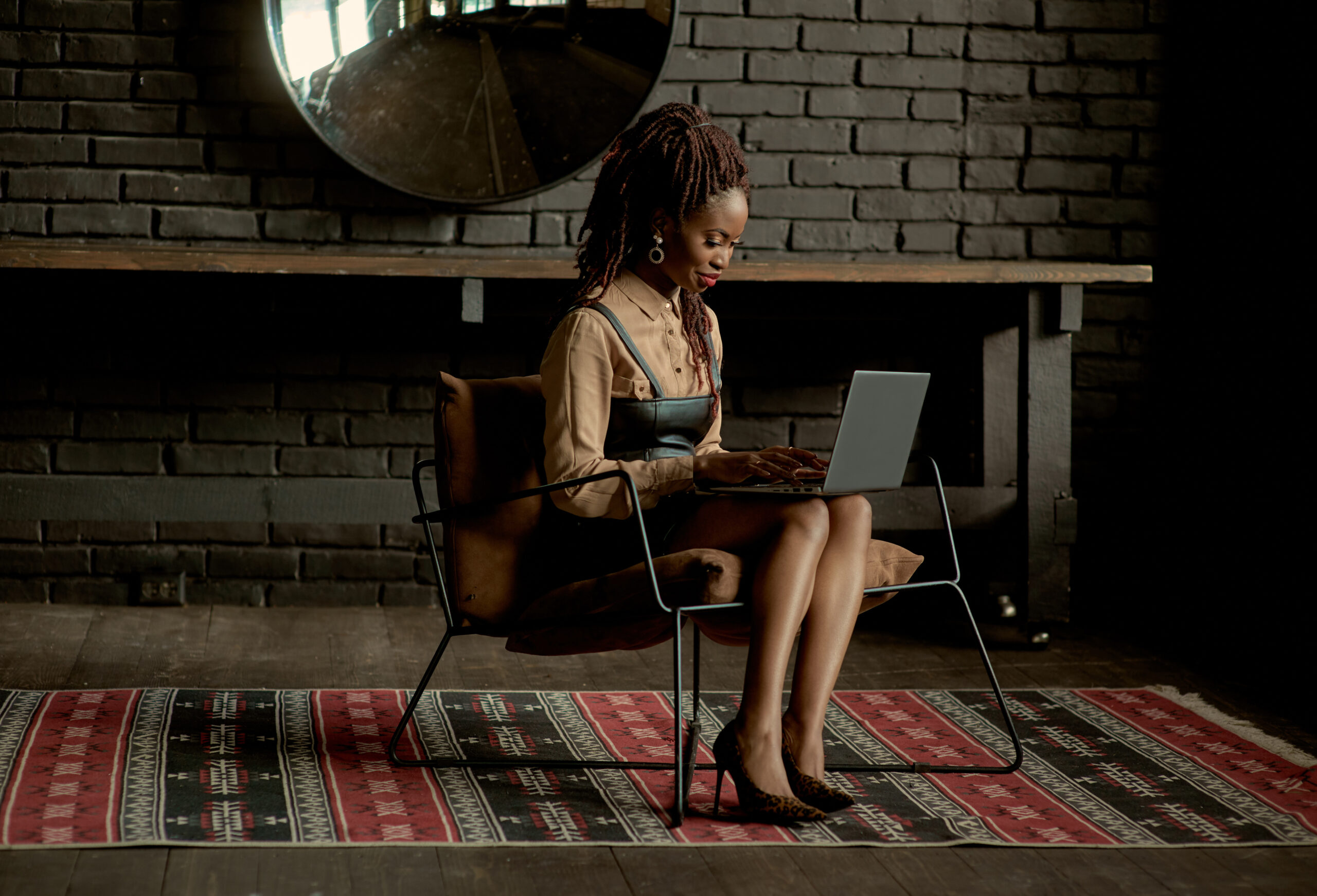 A focused individual participating in a Master Social Media Coaching Programme, attentively working on a laptop in a chic, rustic room with a brick wall background.