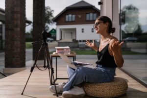 An enthusiastic content creator engaging with her audience through a live video session outdoors, with a professional camera set up on a tripod and a laptop on a small table, embodying the spirit of DIY personal brand content creation.