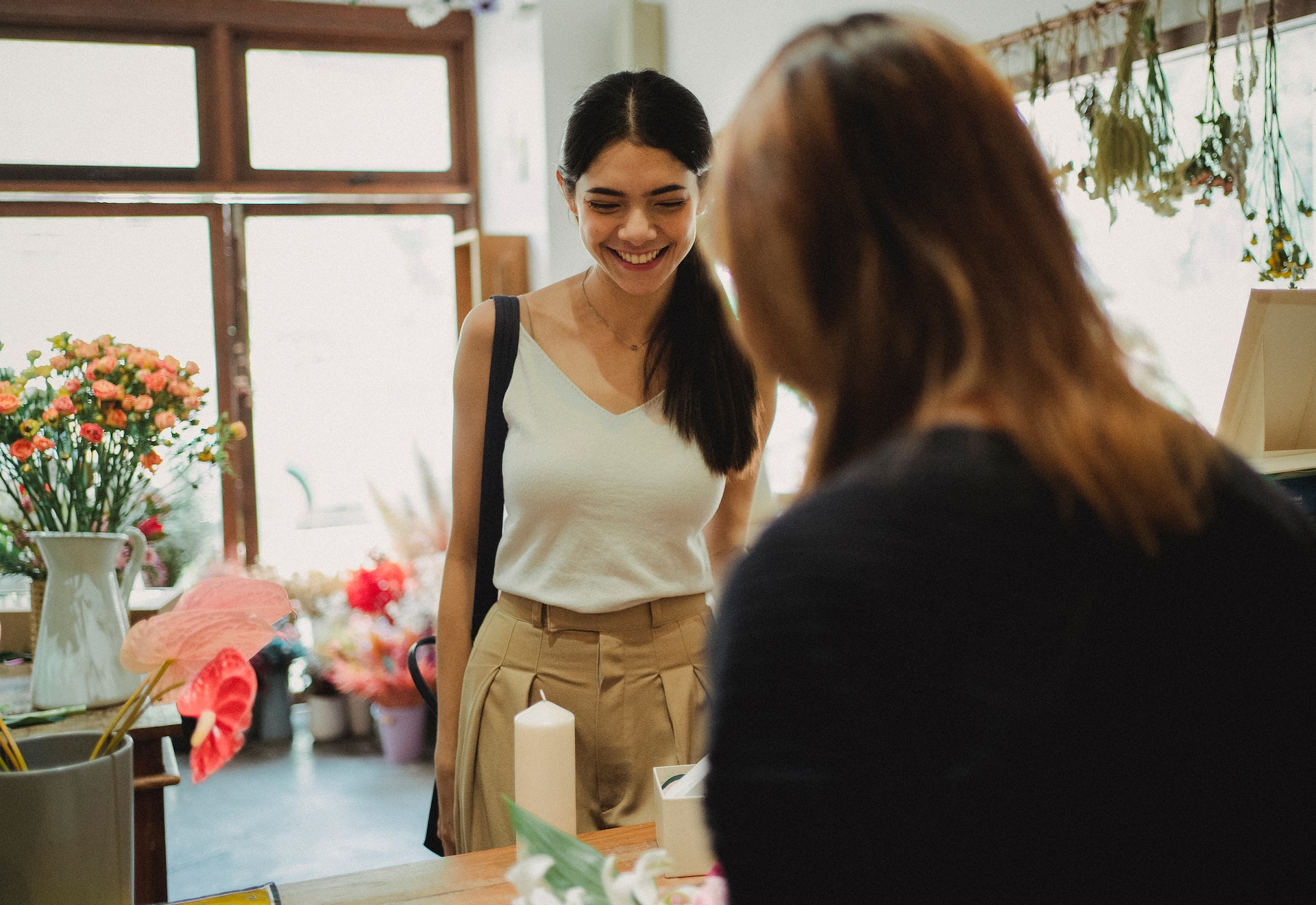 A smiling customer experiencing emotional buying as she happily interacts with a salesperson at a warmly lit, cozy flower shop.