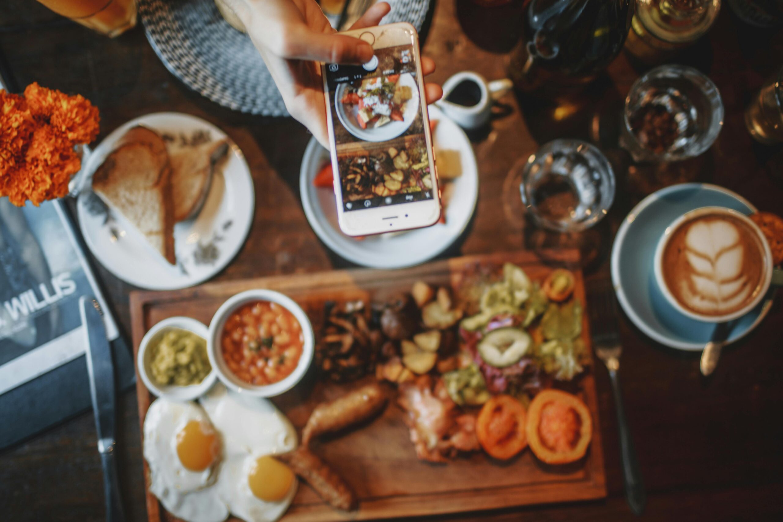 A person capturing their brunch spread on a smartphone, showcasing the essence of finding your content creation strength with a variety of dishes laid out on a wooden table