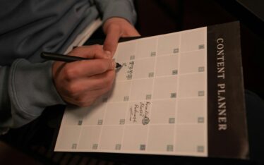 Close-up of hands holding a pen and writing on a 'Content Planner' schedule, emphasizing strategic planning for social media consistency.
