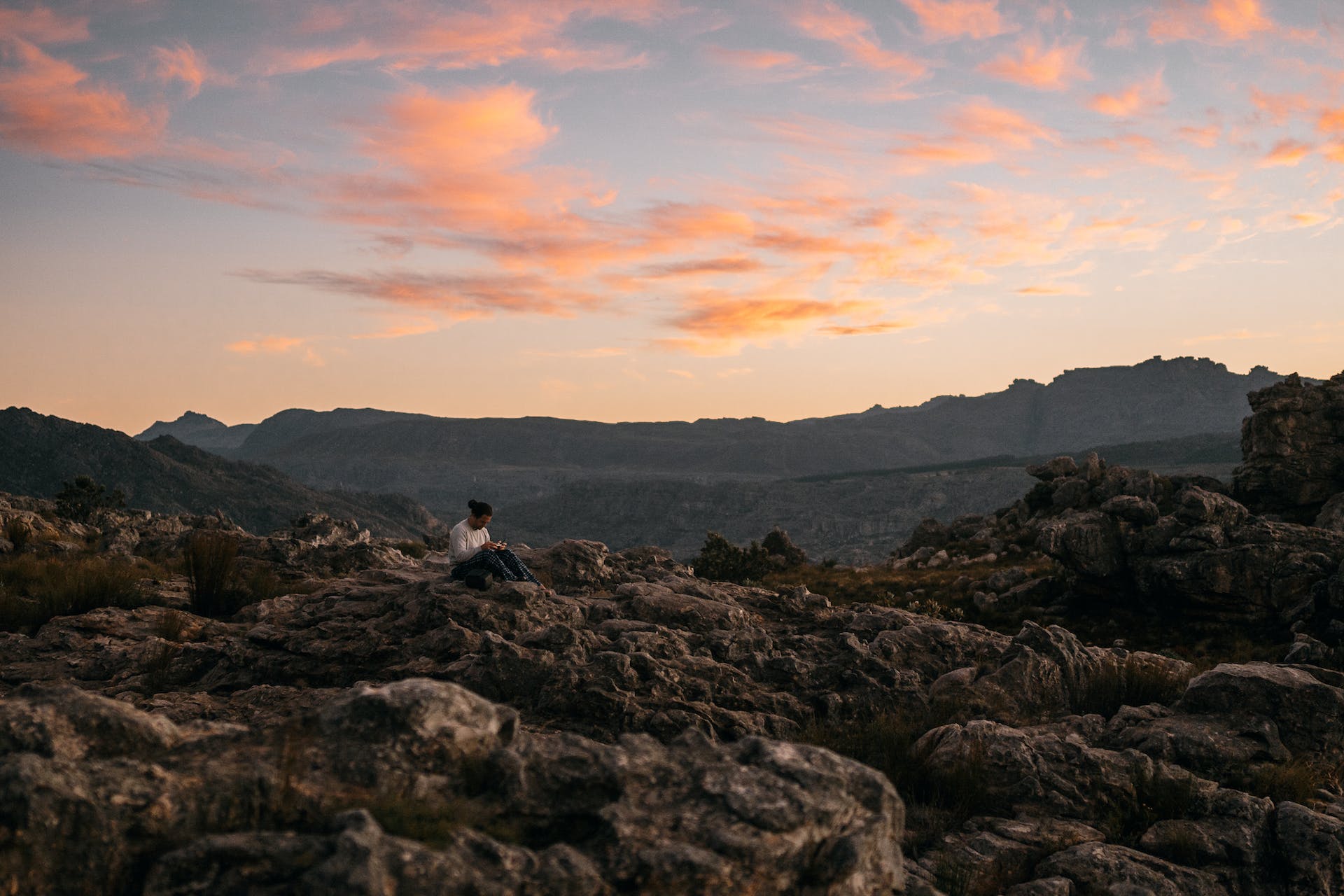 Person sitting peacefully atop a rugged mountain at sunrise, embodying Intentional Energy and personal growth potential.