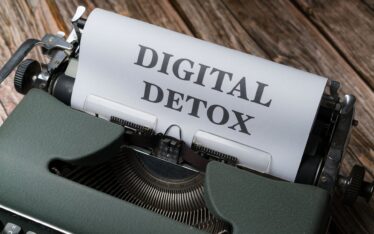A classic typewriter on a wooden background, with a paper prominently displaying the words 'DIGITAL DETOX' in uppercase letters. This image symbolizes the concept of 'Managing Mental Health with Social Media' by taking a step back from digital platforms for mental well-being.