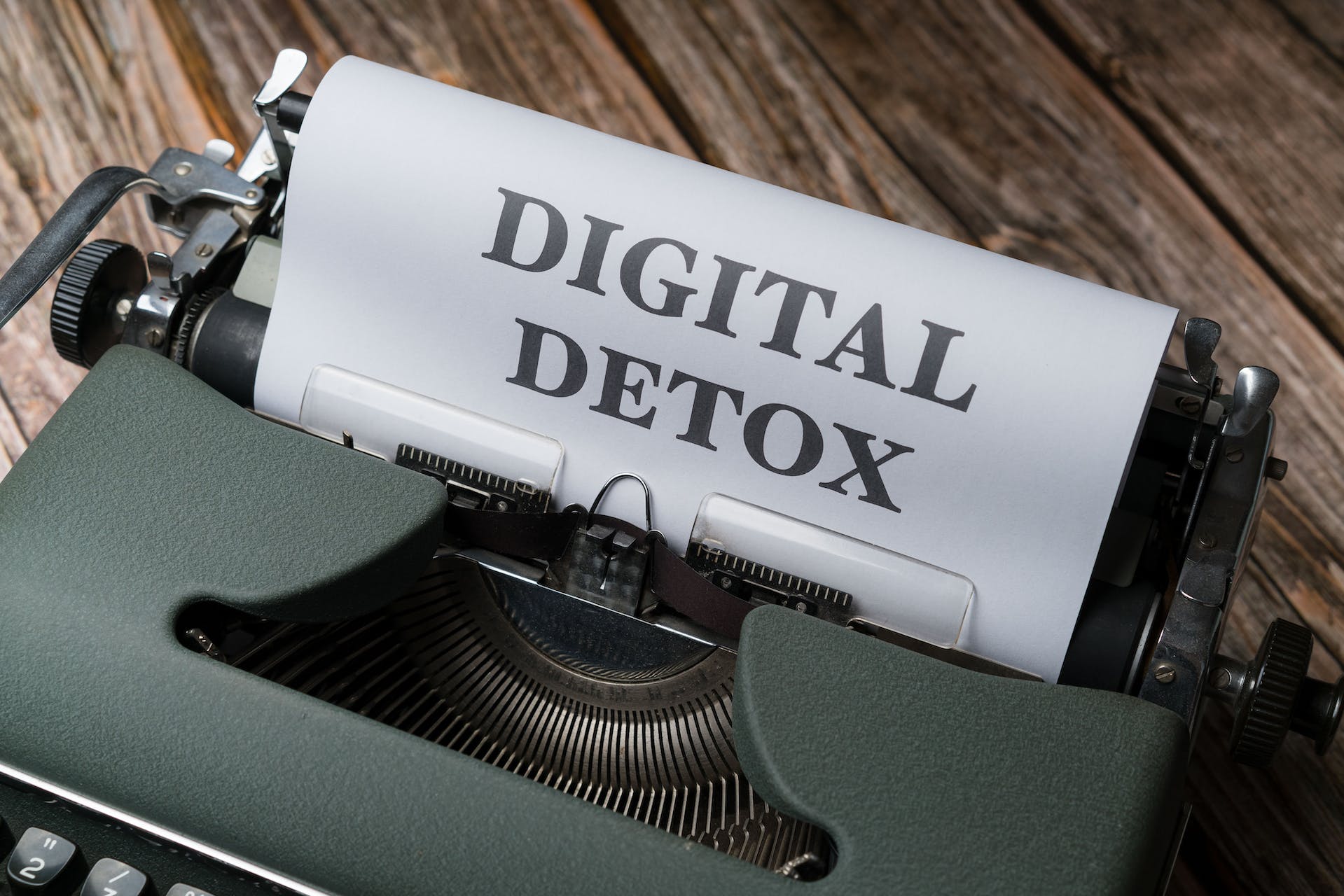 A classic typewriter on a wooden background, with a paper prominently displaying the words 'DIGITAL DETOX' in uppercase letters. This image symbolizes the concept of 'Managing Mental Health with Social Media' by taking a step back from digital platforms for mental well-being.