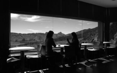 Two individuals engaging in a heartfelt conversation by a large window overlooking a serene mountain landscape, embodying the concept of embracing life.